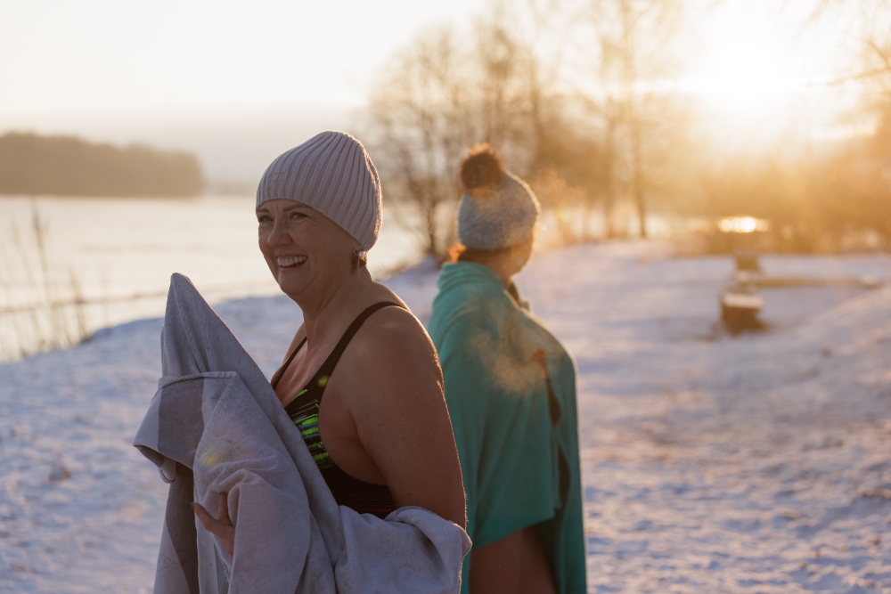 Two women stand at the river's edge as the sun rises, having just finished a winter swim.