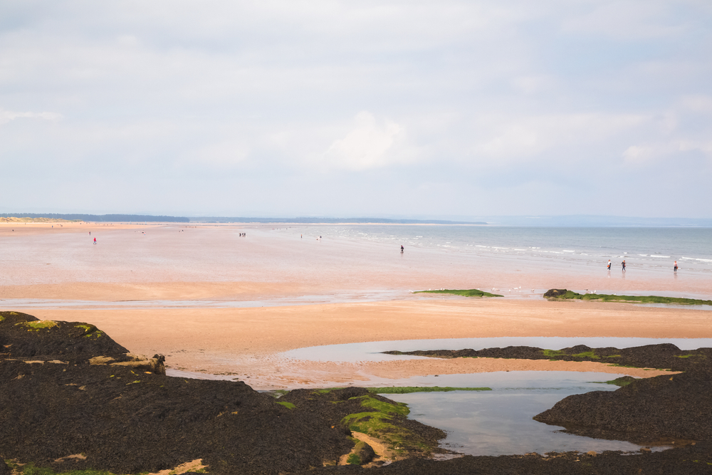 Visitors enjoy a stroll along West Sands Beach at low tide on the North Sea in the seaside town of St Andrews.